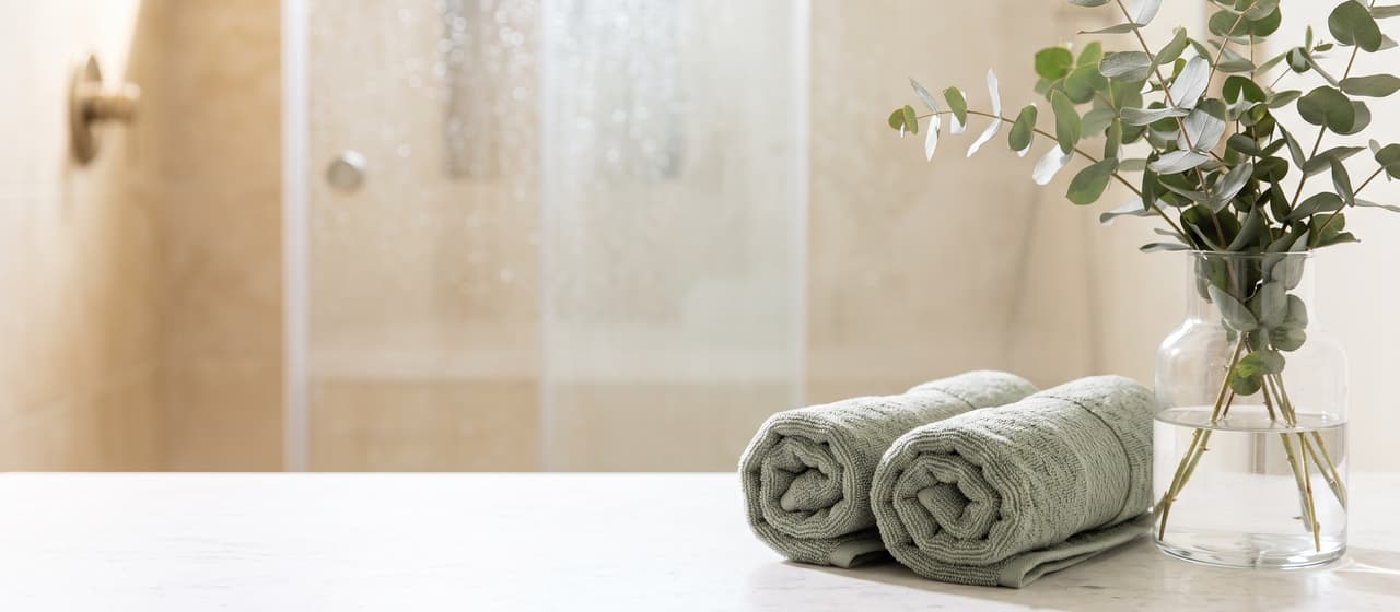 Serviettes roulées vert sauge et eucalyptus devant une douche vitrée couverte de gouttes